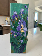 Palette knife impasto painting of purple flowers on a green background, placed on a white surface.