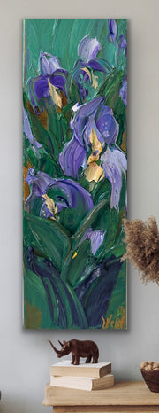 Palette knife impasto painting of purple flowers on a light gray wall with decorative items below.