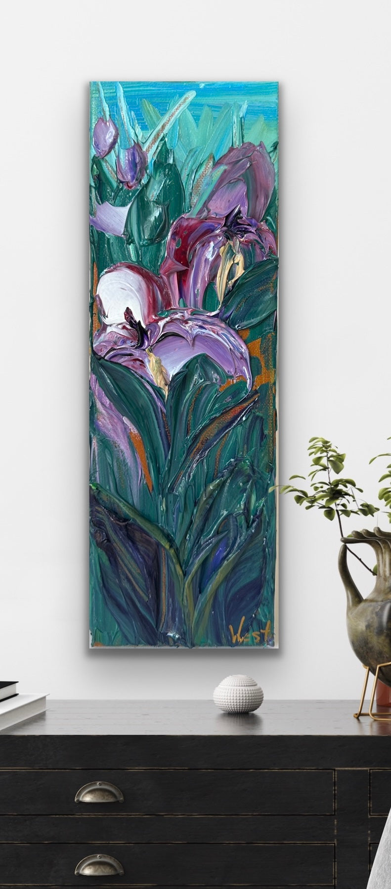 Palette knife impasto painting of purple flowers on a white wall above a dark wooden dresser.