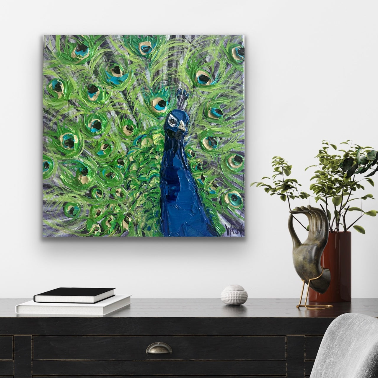 Painting of a peacock with green feathers and a blue head on a wall above a desk.