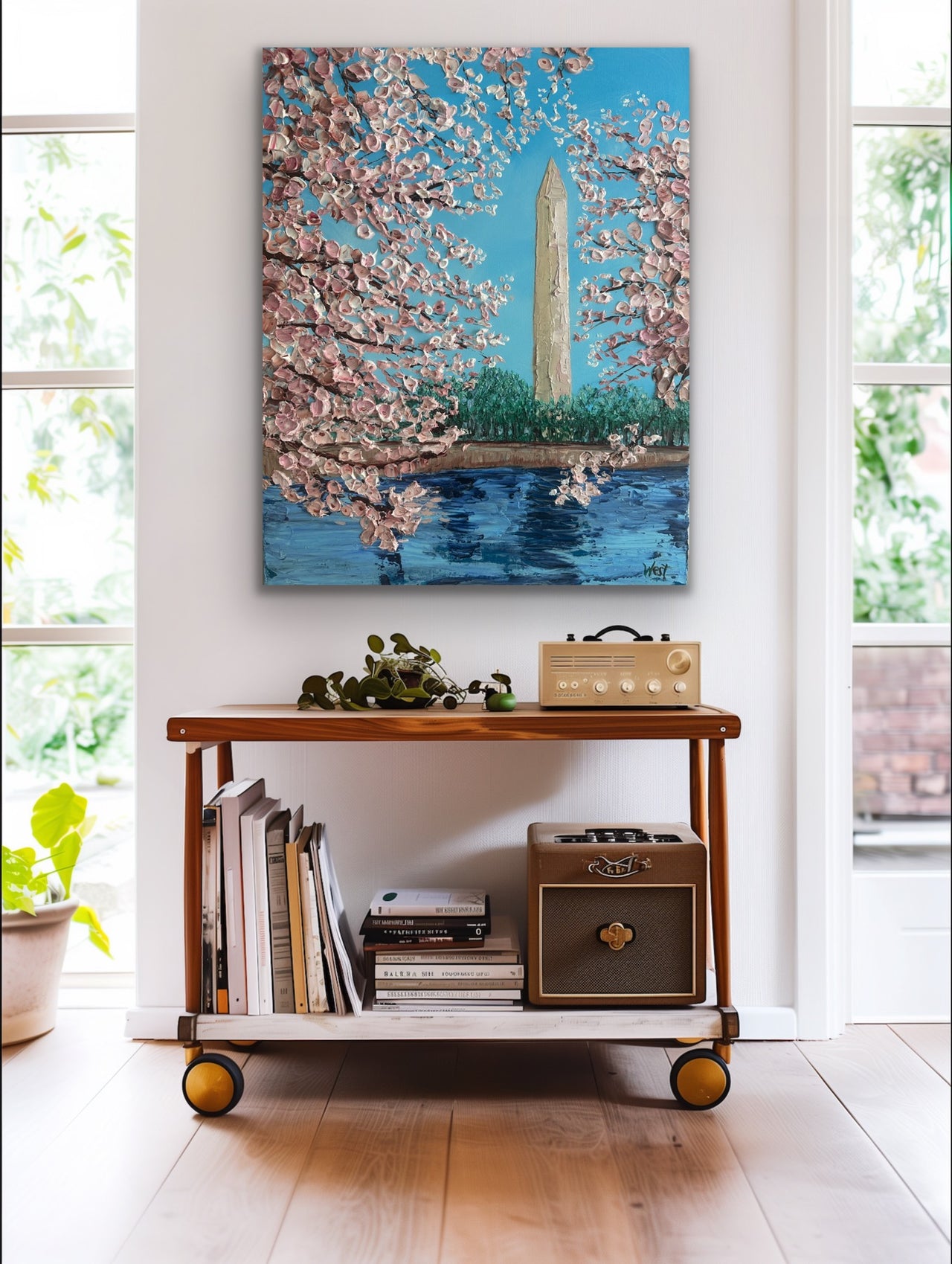 Cart with books and a plant in a room with a painting of cherry blossoms and a monument.