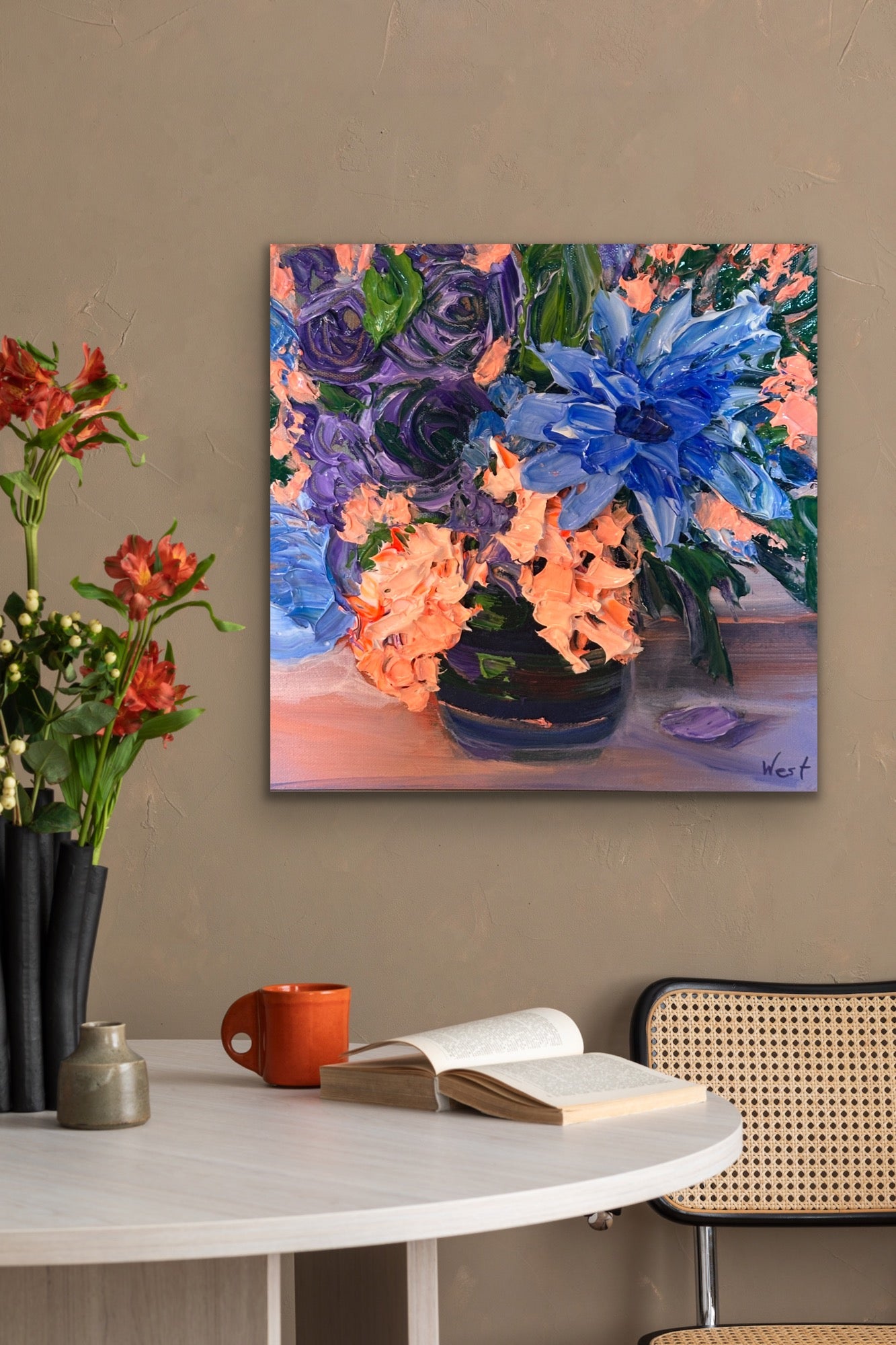 Floral palette knife painting on a wall above a table with a book and mug.