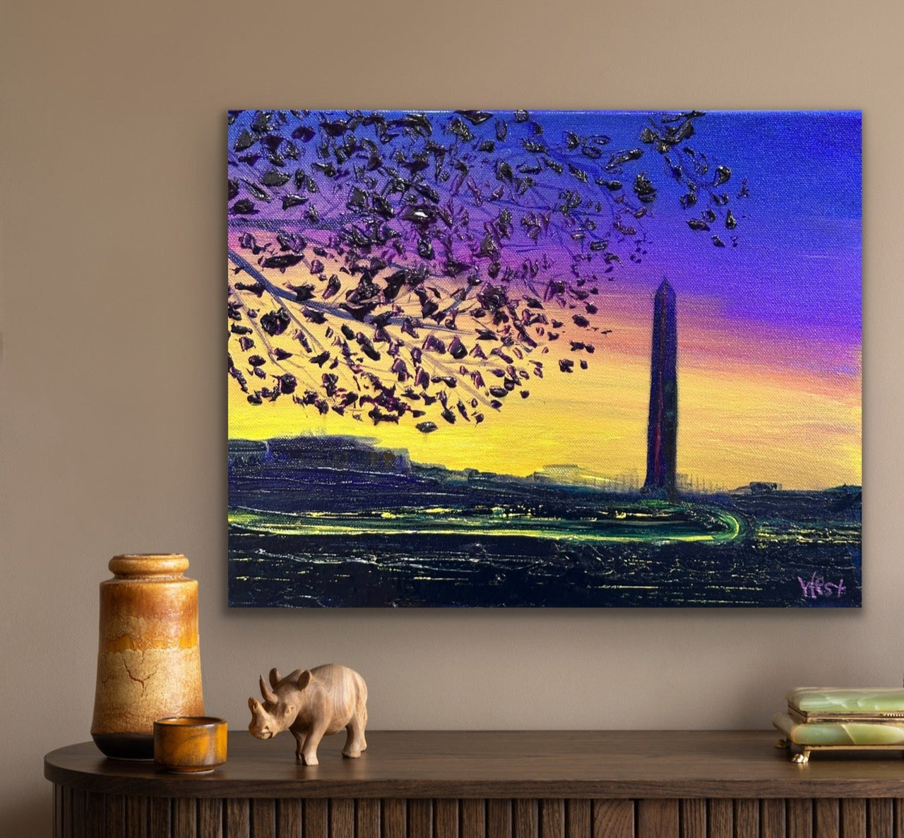 Painting of the Washington Monument with birds flying over a purple sky on a beige wall.